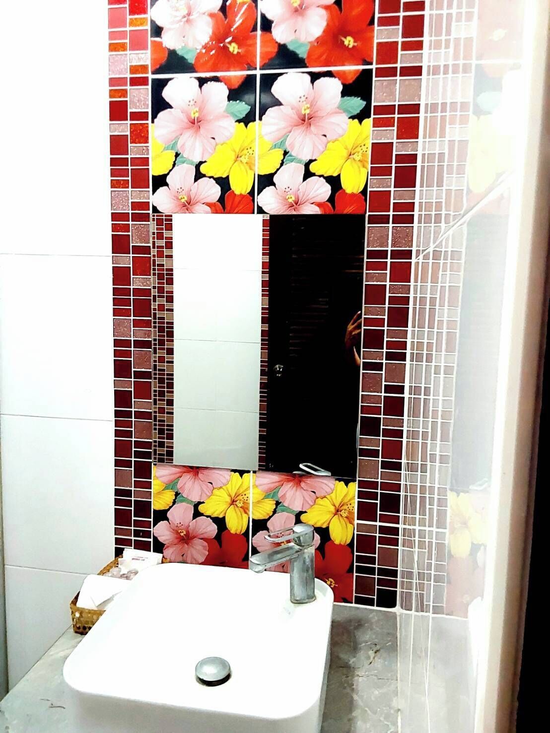 A bathroom with a white sink, a mirror, and a tiled wall with floral patterns.