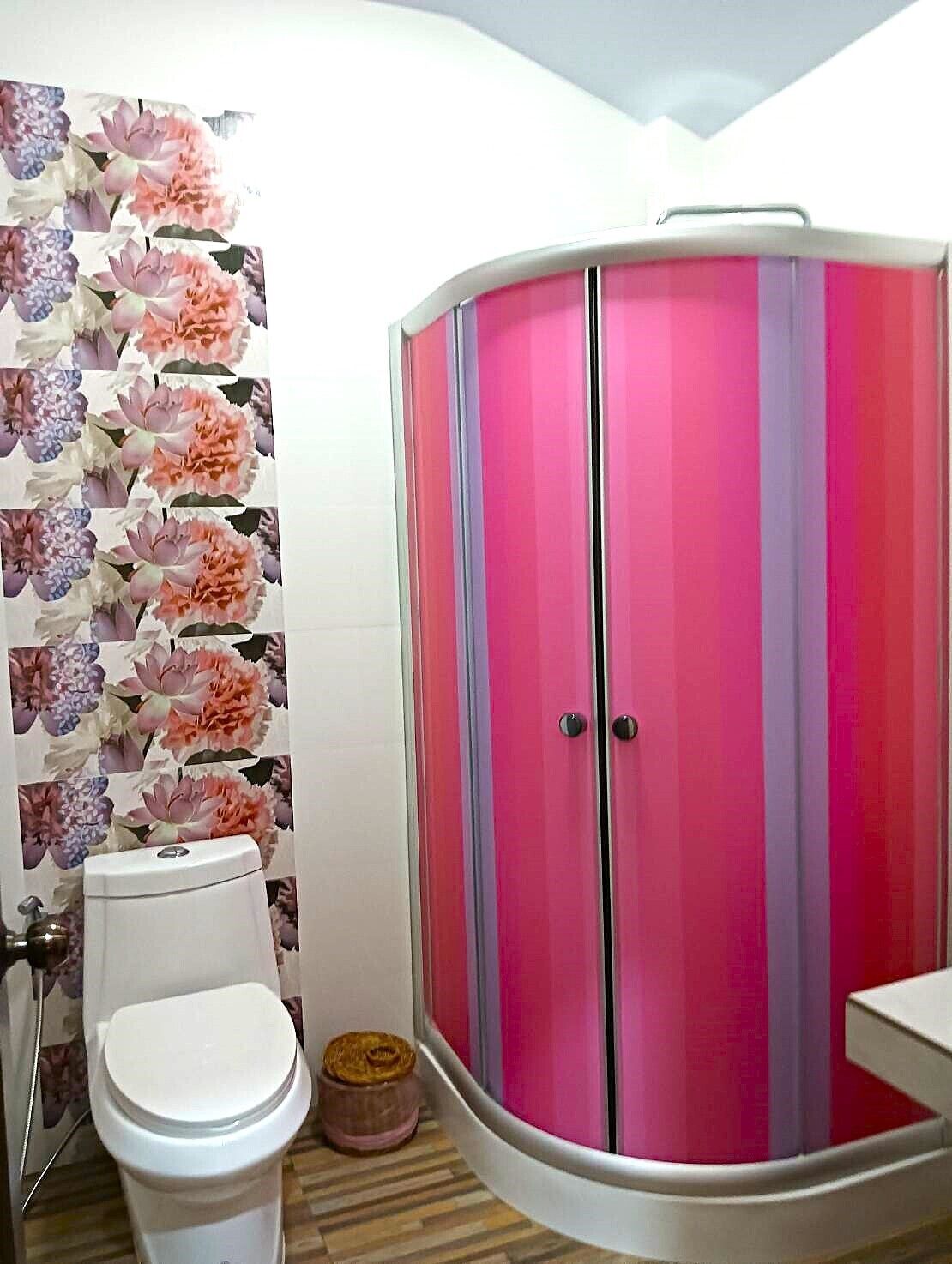 A bathroom with a white toilet, a pink and purple wardrobe, and a floral wallpaper.