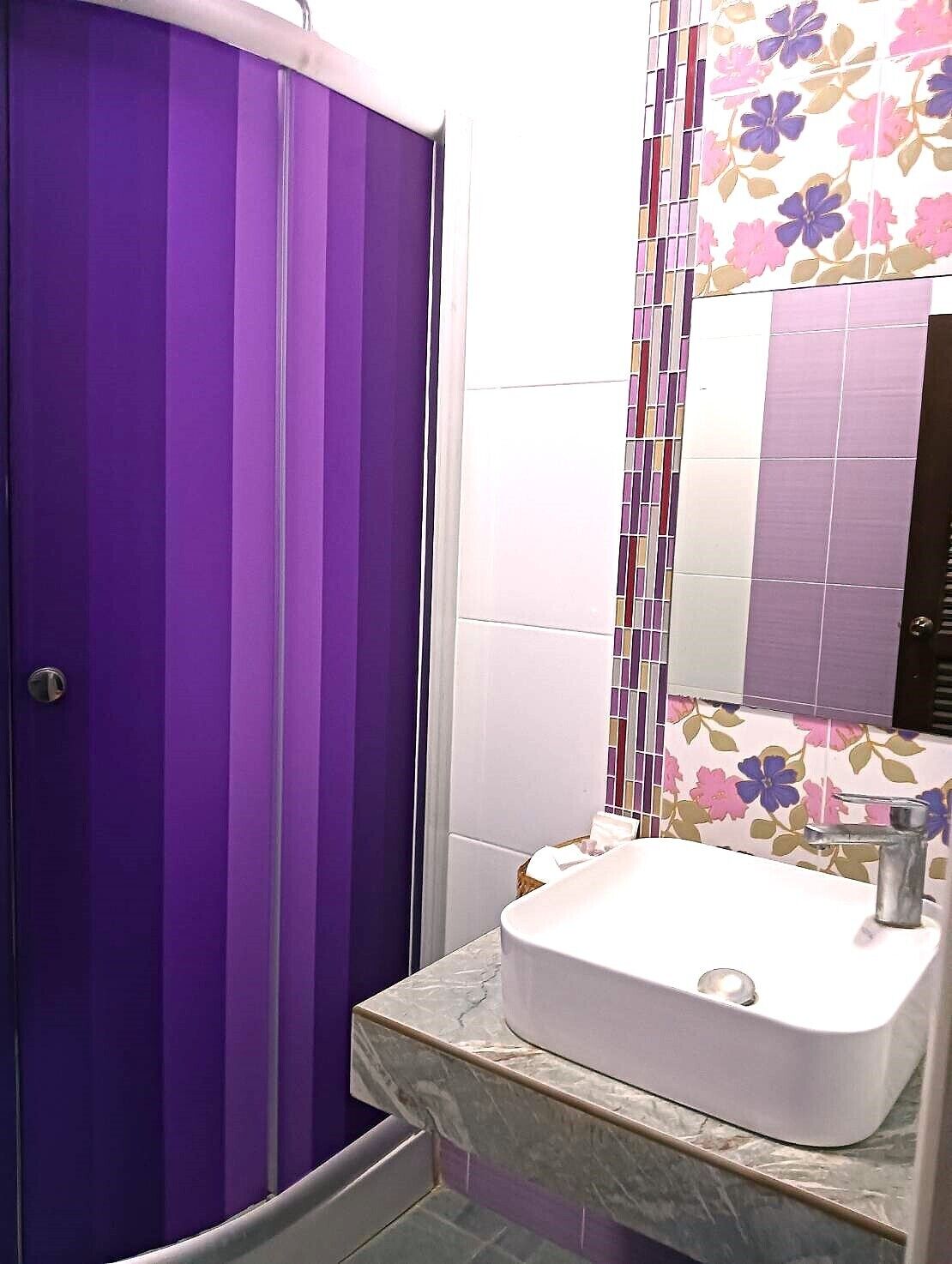 A bathroom with a purple door, a white sink, and a mirror with floral tiles.