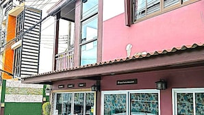 A two-story building with a storefront, a car parked in front, and a person standing near the entrance.