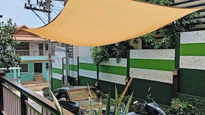 A residential area with a parked car and a motorcycle, a yellow shade sail, and a green wall with a patterned design.