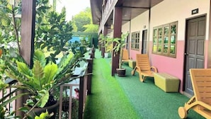 A covered outdoor area with artificial turf, wooden lounge chairs, and potted plants.
