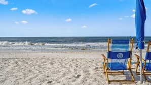 A beach with two blue beach chairs and a matching umbrella. - Phoenix 8 903 | Indoor, Outdoor Pools | Beachfront | Tennis | My Beach Getaways (Orange Beach)
