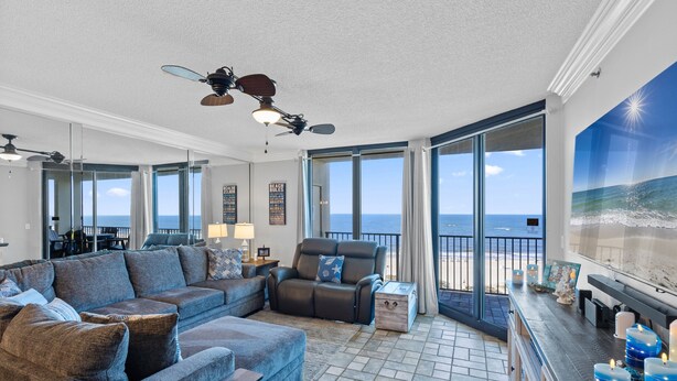 A spacious living room with a large sectional sofa, a recliner, and a coffee table. There are multiple windows offering a view of the ocean. - Phoenix 8 903 | Indoor, Outdoor Pools | Beachfront | Tennis | My Beach Getaways (Orange Beach)