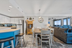 A modern kitchen with white cabinets, a blue bar area, and a dining table with white chairs. - Phoenix 8 903 | Indoor, Outdoor Pools | Beachfront | Tennis | My Beach Getaways (Orange Beach)