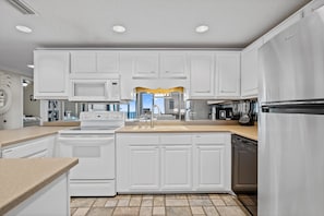 A modern kitchen with white cabinets, a stainless steel refrigerator, and a built-in oven. - Phoenix 8 903 | Indoor, Outdoor Pools | Beachfront | Tennis | My Beach Getaways (Orange Beach)