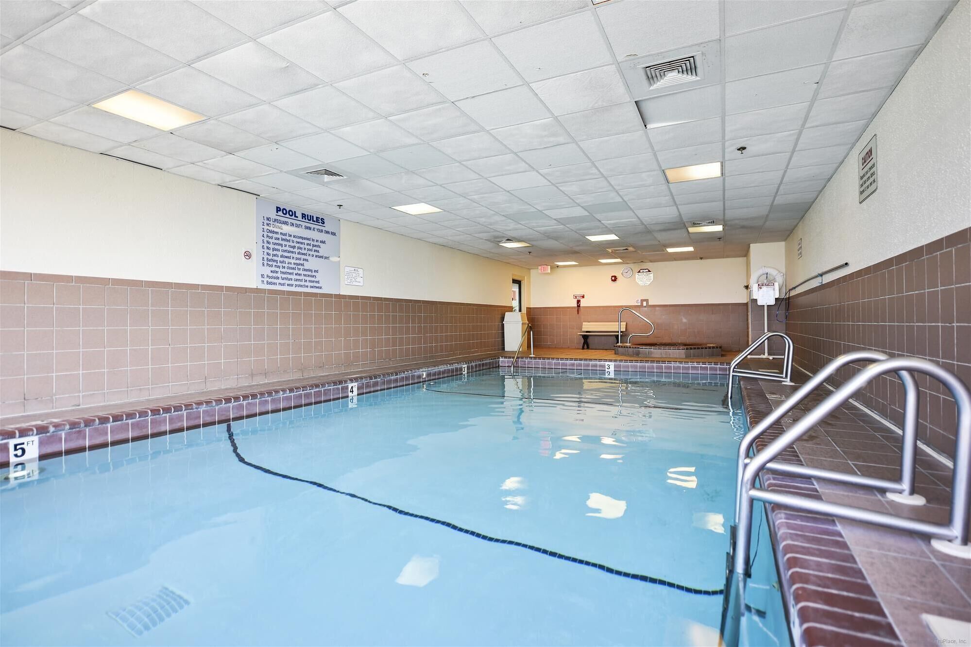 An indoor swimming pool with clear water, tiled walls, and a sign listing pool rules.