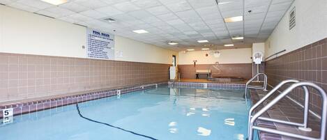 An indoor swimming pool with clear water, tiled walls, and a sign listing pool rules.