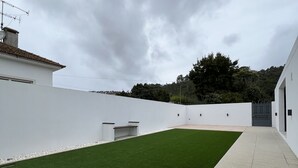 Un espacio exterior moderno con césped artificial, un sendero pavimentado y paredes blancas.