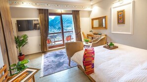 Ett hotellrum med en säng, ett skrivbord, en stol, en TV, ett fönster med utsikt över bergen och en balkong.