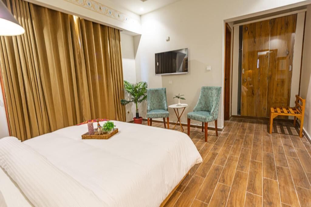 A hotel room with a large bed, two armchairs, a small table, and a TV on the wall.