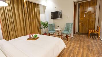 A hotel room with a large bed, two armchairs, a small table, and a TV on the wall.