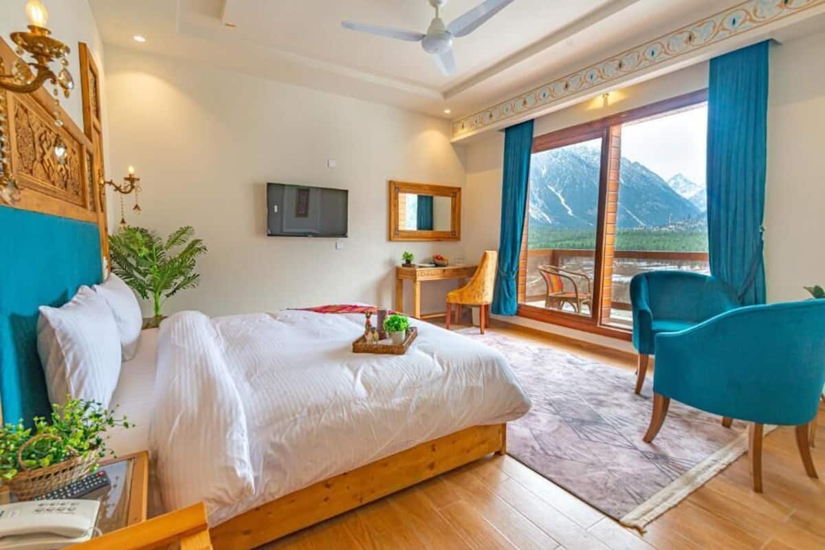 Habitación de hotel con cama, escritorio, silla, televisión y balcón con vista a la montaña.