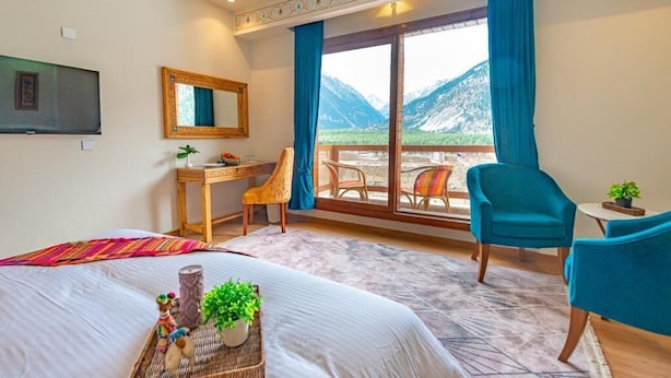 Ett hotellrum med en säng, ett skrivbord, en stol, en TV och en balkong med utsikt över bergen.