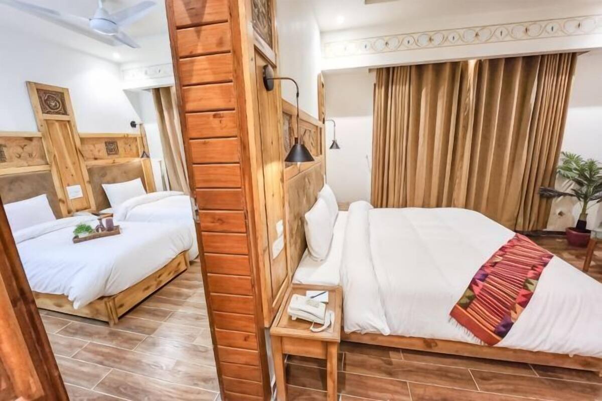 Habitación de hotel con dos camas, cabeceros de madera, una mesita de noche con lámpara, teléfono y una planta.