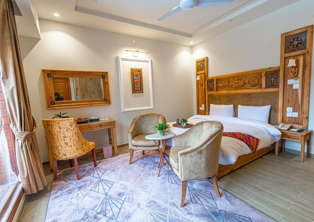 Una camera d'albergo con un letto grande, due poltrone, un tavolino, una ventola a soffitto e una testiera decorativa.
