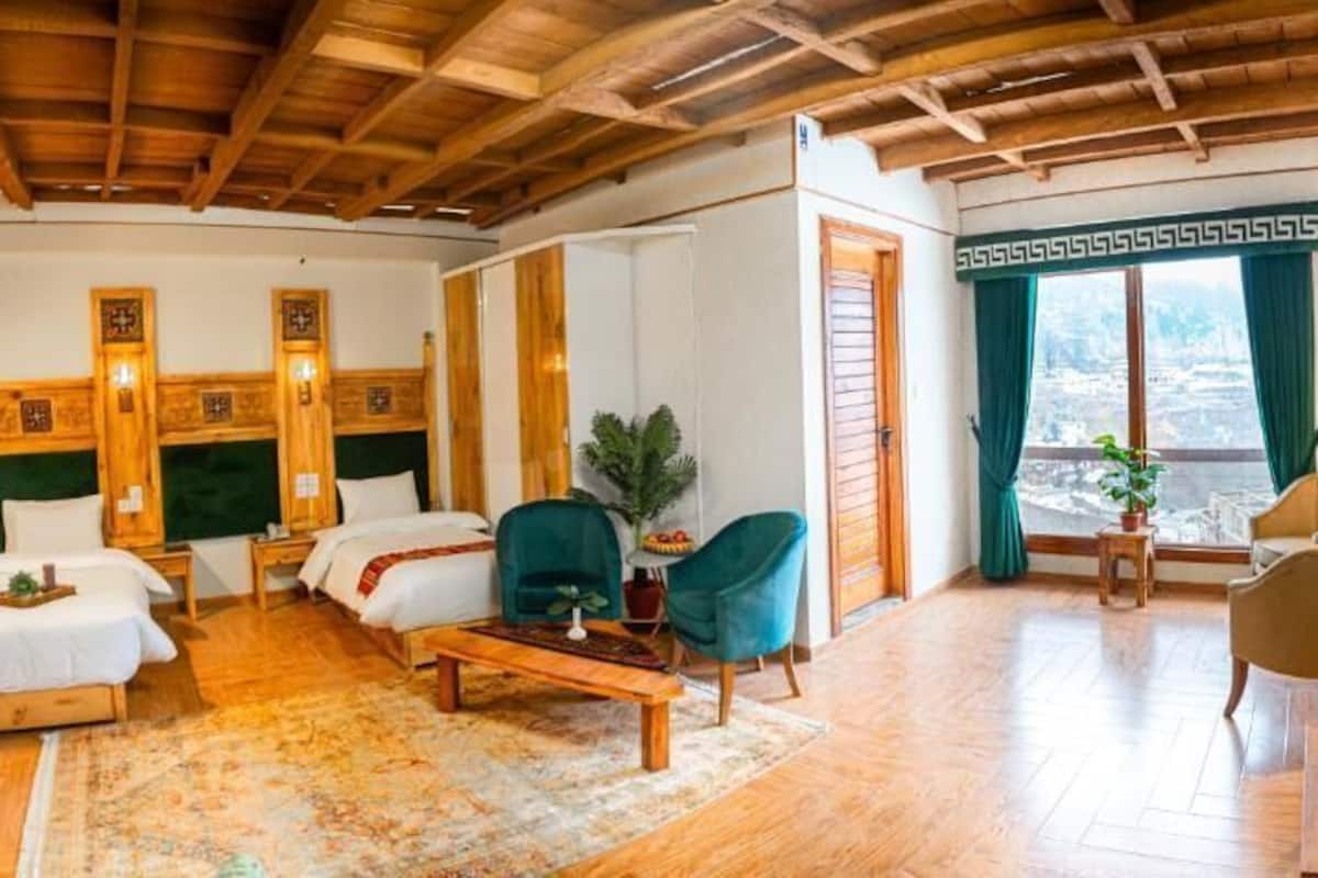 Habitación de hotel con dos camas, techo de madera, un ventanal grande con cortinas y un televisor en la pared.