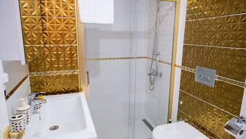 Um banheiro com chuveiro em box de vidro, pia branca e vaso sanitário.