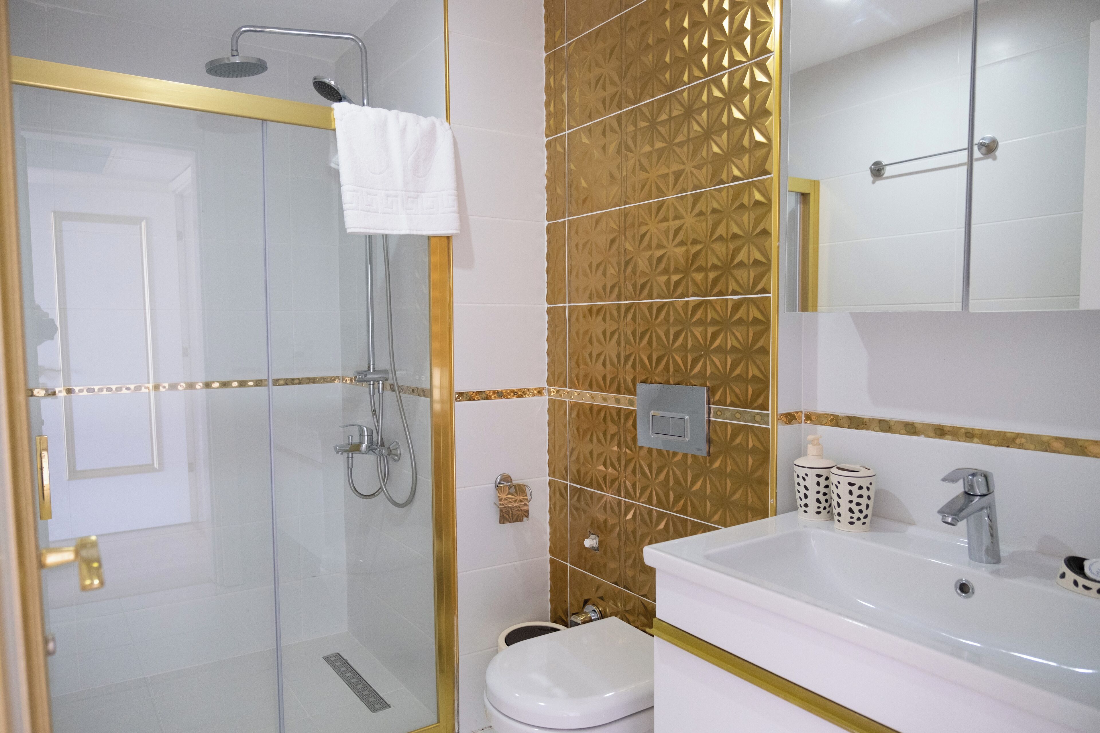 Ein modernes Badezimmer mit einer Duschkabine, einem weißen Waschbecken und Fliesen mit Goldmuster.