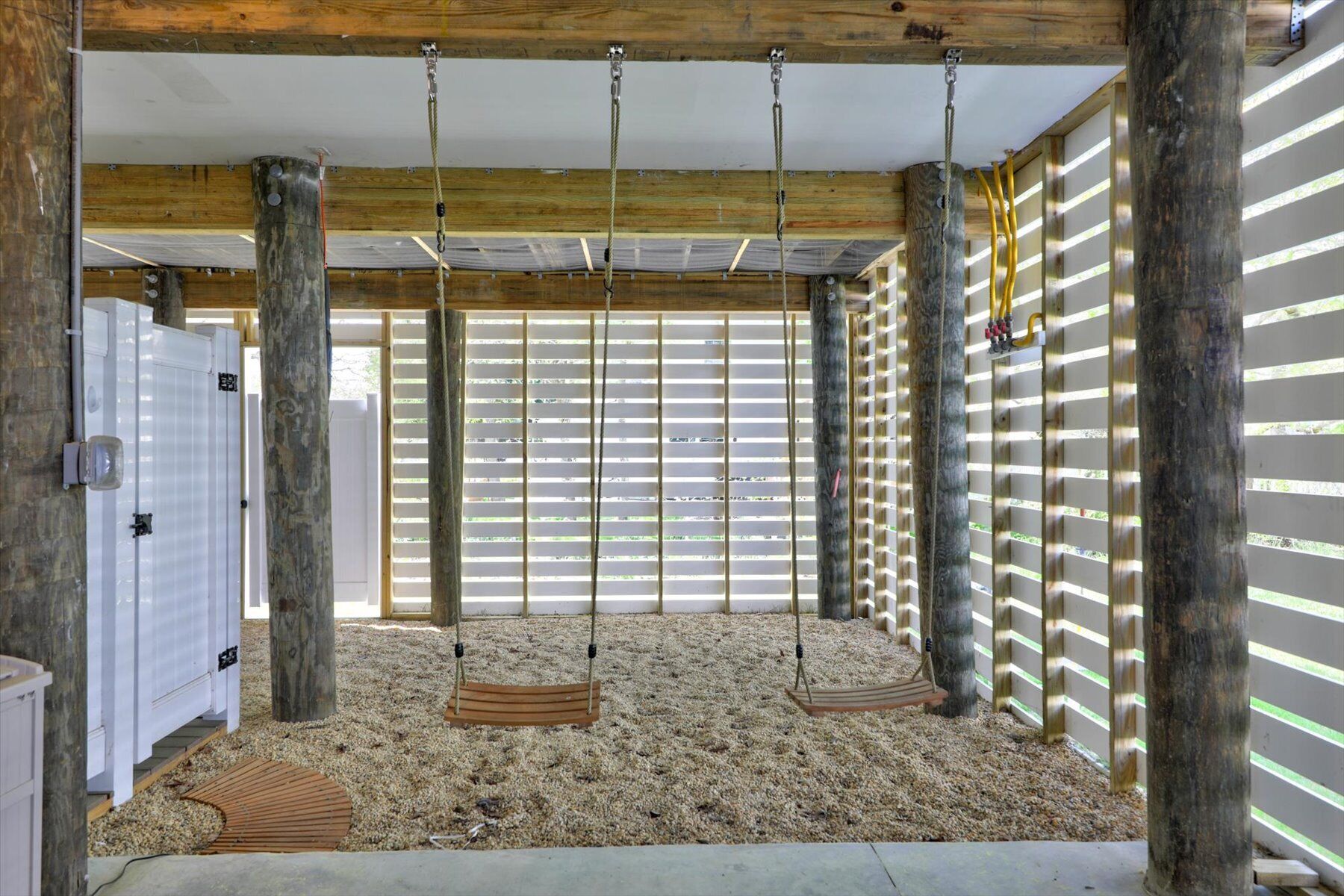 A room with a wooden ceiling, a swing set, a white door, and a window with blinds.