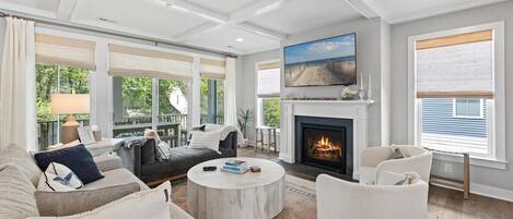 A spacious living room with a fireplace, comfortable seating, and large windows offering views of the outdoors.