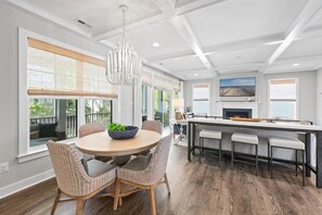 A modern kitchen with a round dining table, wicker chairs, a chandelier, and a fireplace. - 5BR Beauty Near Bethany-Community Pool; Linens (Ocean View)