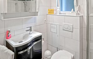 Ein Badezimmer mit einem weißen Waschbecken, einem Spiegel darüber, einem Handtuchhalter, einer Toilette und einer Duschkabine.