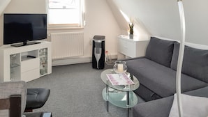 Een moderne woonkamer met een flatscreen televisie, een glazen salontafel, een grijze bank en een radiator.
