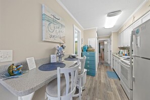 Una cucina con piano di lavoro in granito, sedie bianche, un armadietto blu e un frigorifero.