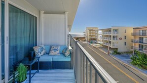 A balcony with a sofa and cushions, overlooking a street with buildings and a clear sky. - Private Pool Steps From the Beach (Ocean City)