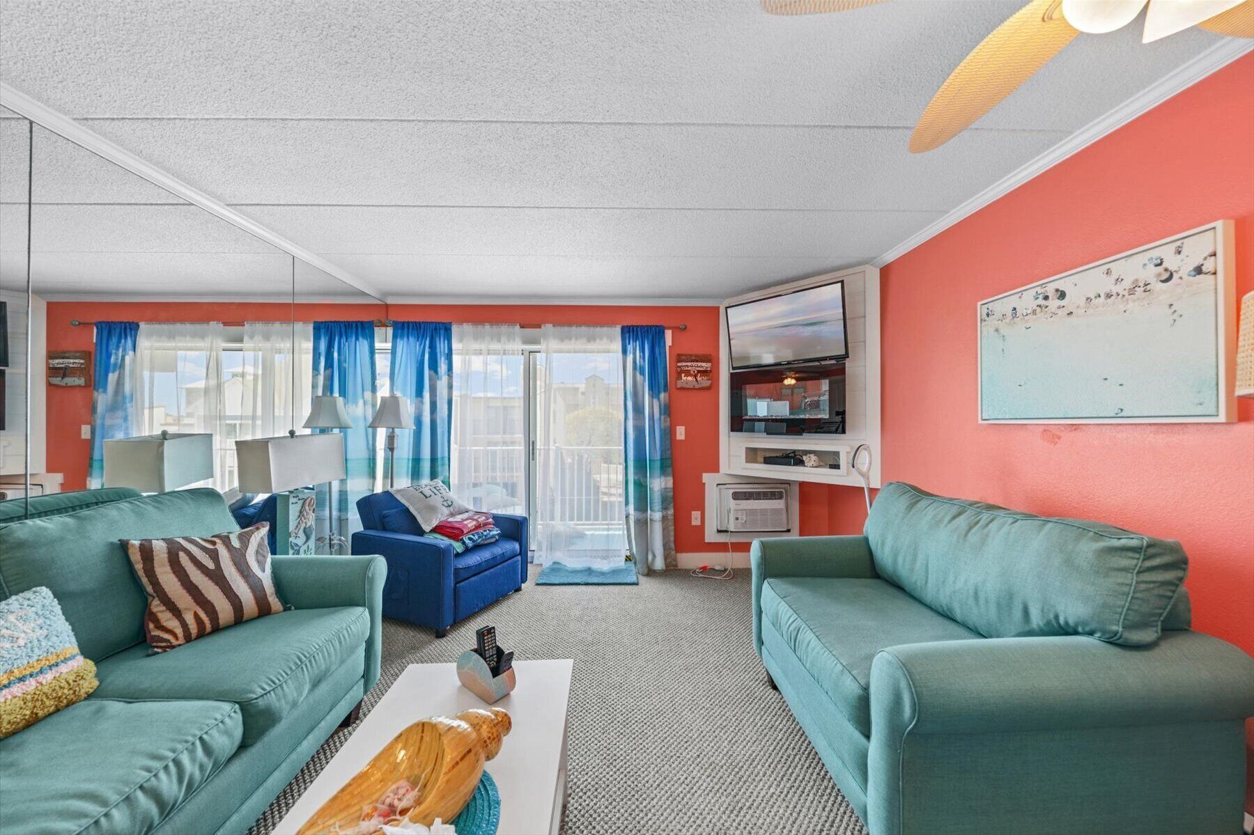 Un salon avec des canapés de couleur turquoise, une table basse blanche et un téléviseur posé sur un meuble blanc.