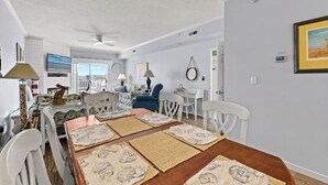 Un comedor con una mesa de madera, sillas blancas y individuales tejidas.