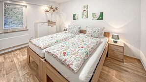Una cama doble con ropa de cama floral, una mesita de noche con lámpara y una obra de arte colgada en la pared.