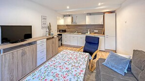 Un espacio habitable compacto con cama, sofá, televisor, kitchenette y comedor.