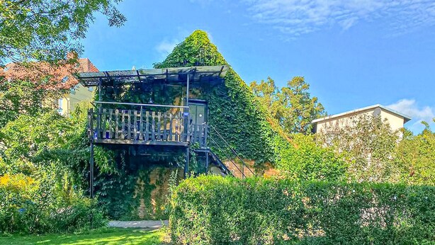 Un jardín con una estructura singular que incluye un balcón de vidrio y un techo cónico.