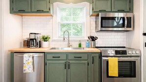 A kitchen with green cabinets, a stainless steel refrigerator, a microwave, a stove, and a window with a view of trees. - Relaxing historic home close to Churchill Downs! (Louisville)