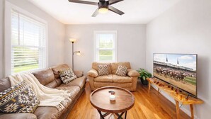 A living room with two leather sofas, a round wooden coffee table, a ceiling fan, and a mounted TV displaying a horse race. - Relaxing historic home close to Churchill Downs! (Louisville)