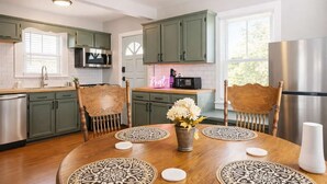 A modern kitchen with green cabinets, a stainless steel refrigerator, and a dining table with ornate chairs and patterned placemats. - Relaxing historic home close to Churchill Downs! (Louisville)