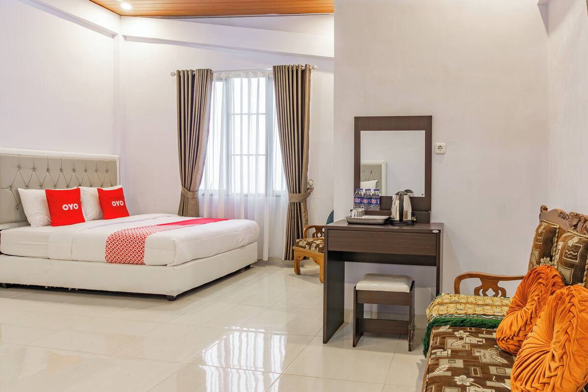 A hotel room with a bed, a desk, a chair, a mirror, and a window with curtains.
