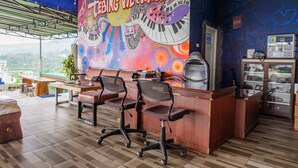 A restaurant with a colorful mural, two office chairs, a wooden counter, and a view of the city. - Hotel O Tebing Vieatnam (Bandar Lampung)