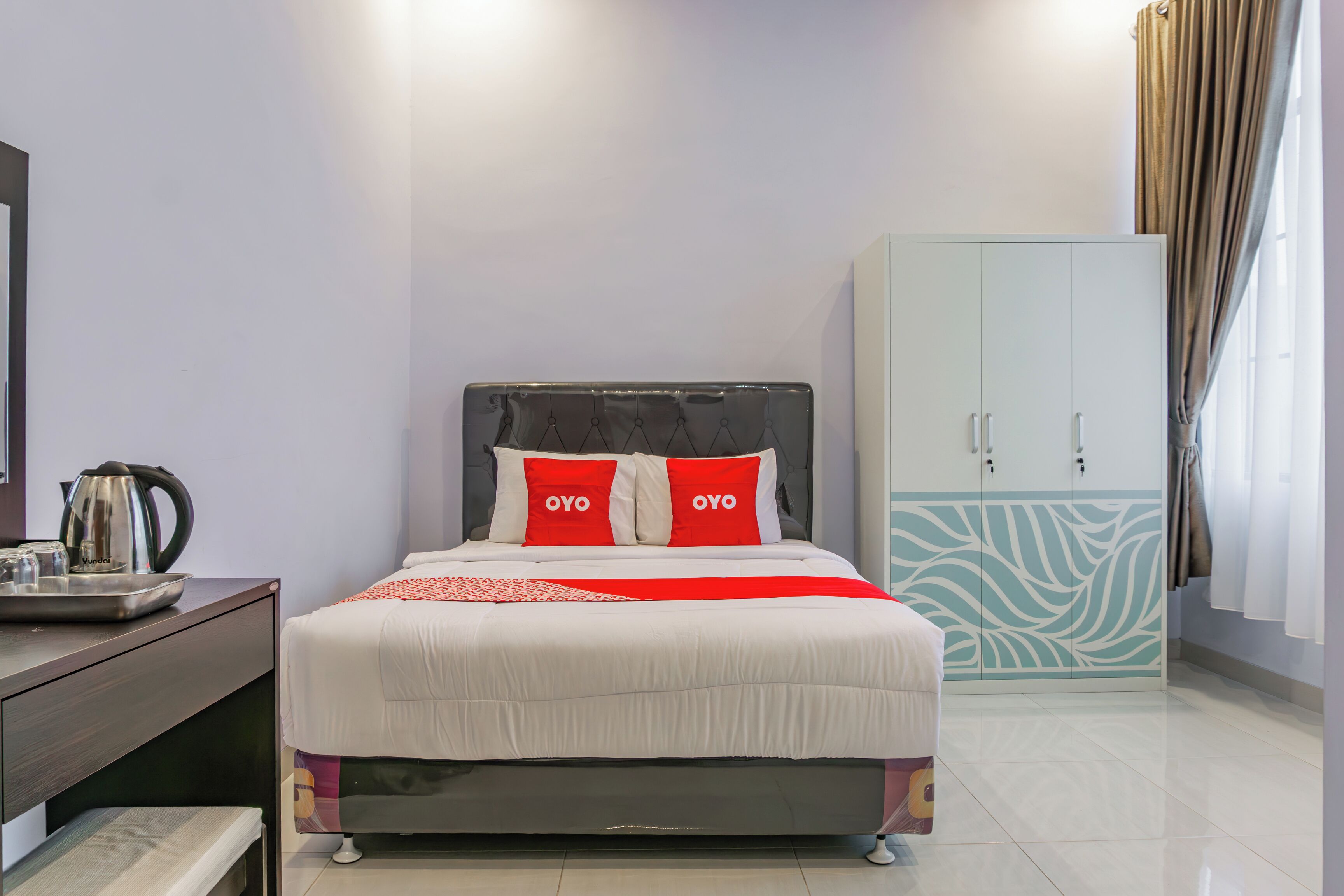A neatly arranged hotel room with a bed, a wardrobe, and a desk with a kettle.