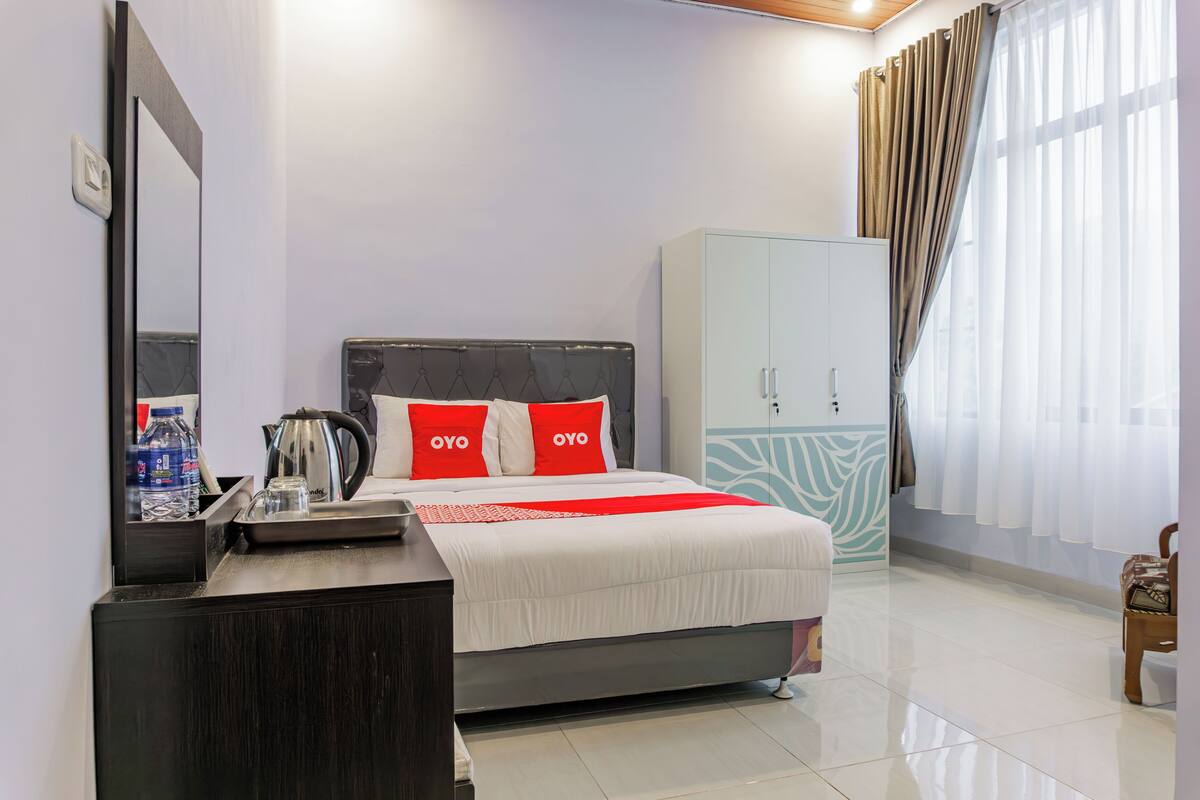 A modern hotel room with a bed, a wardrobe, a mirror, and a bedside table with a kettle and water bottle.