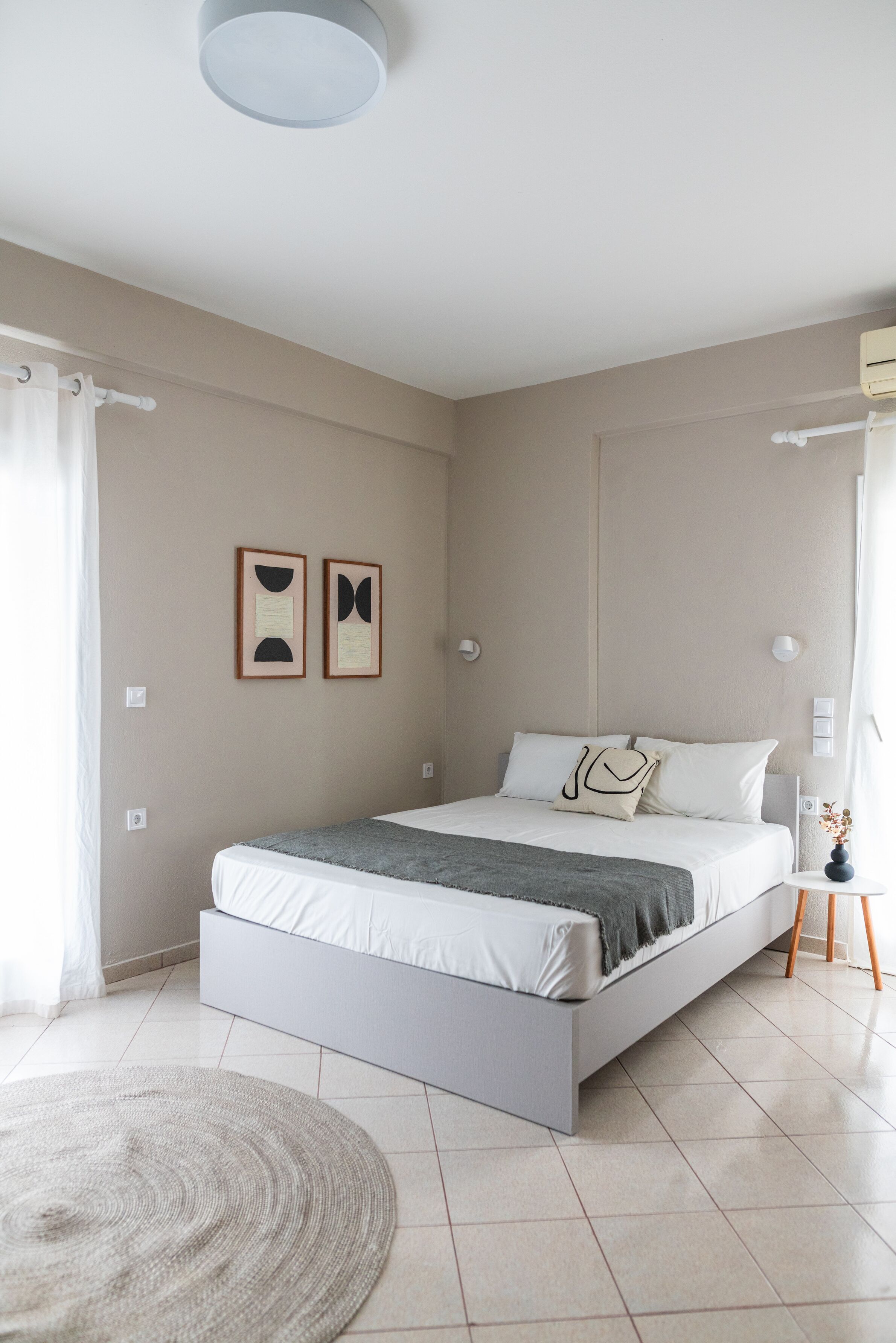 A modern bedroom with a bed, a round rug, and two wall art pieces.