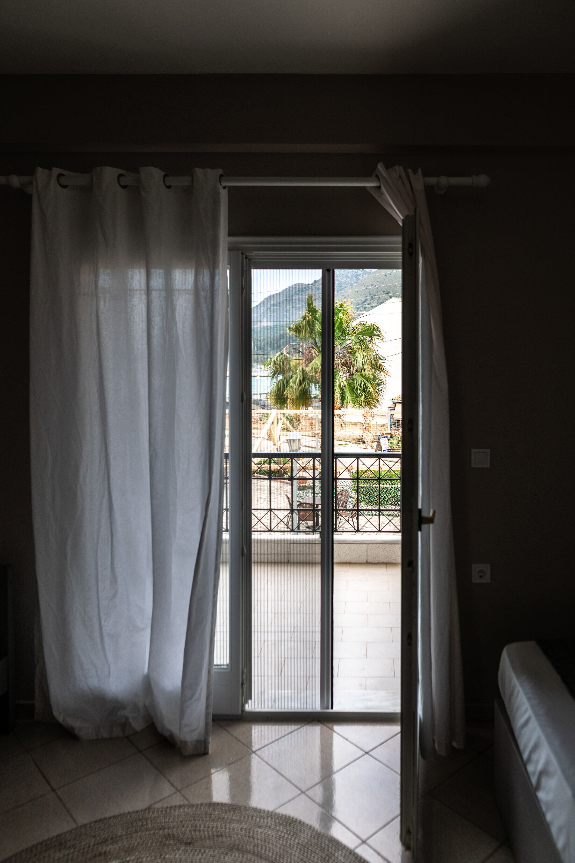 A room with a sliding glass door leading to an outdoor area with a view of palm trees and mountains.