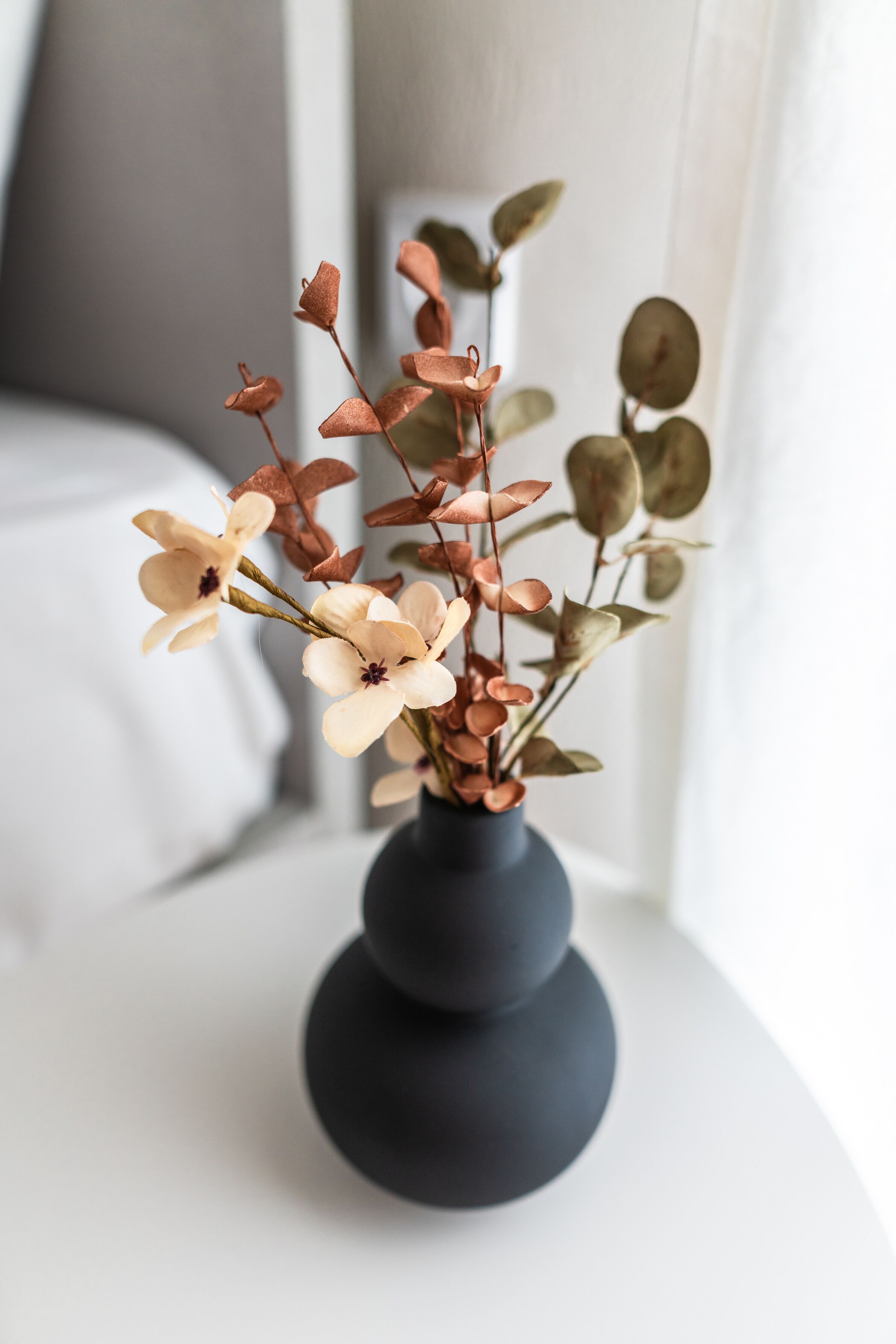 Un florero con flores y hojas sobre una superficie blanca.