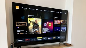 A television mounted on a wooden shelf with a remote control, a decorative vase, and a power strip below. - Entre Loire et Château (Amboise)