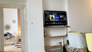 A modern living room with a flat-screen TV mounted on the wall, a round wooden coffee table with wine glasses and a bottle, and a yellow armchair. - Entre Loire et Château (Amboise)