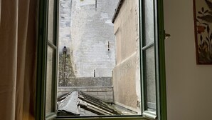 A room with a bed, a bedside lamp, and a window overlooking a historic building. - Entre Loire et Château (Amboise)