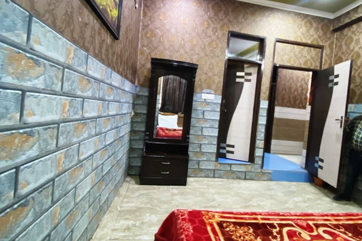A bedroom with a brick-patterned wall, a bed with a red and gold bedspread, a mirror, and a ceiling fan.