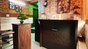 A reception area with a reception desk, a potted plant, a clock, and a framed picture on the wall. - Manali Hotel By GRB (New Delhi)